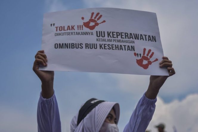 
 Seorang tenaga kesehatan membentangkan poster saat berunjuk rasa menolak RUU Omnibuslaw Kesehatan di depan Gedung Parlemen, Senayan, Jakarta, Senin (28/11/2022). Foto: Sulthony Hasanuddin/Antara Foto